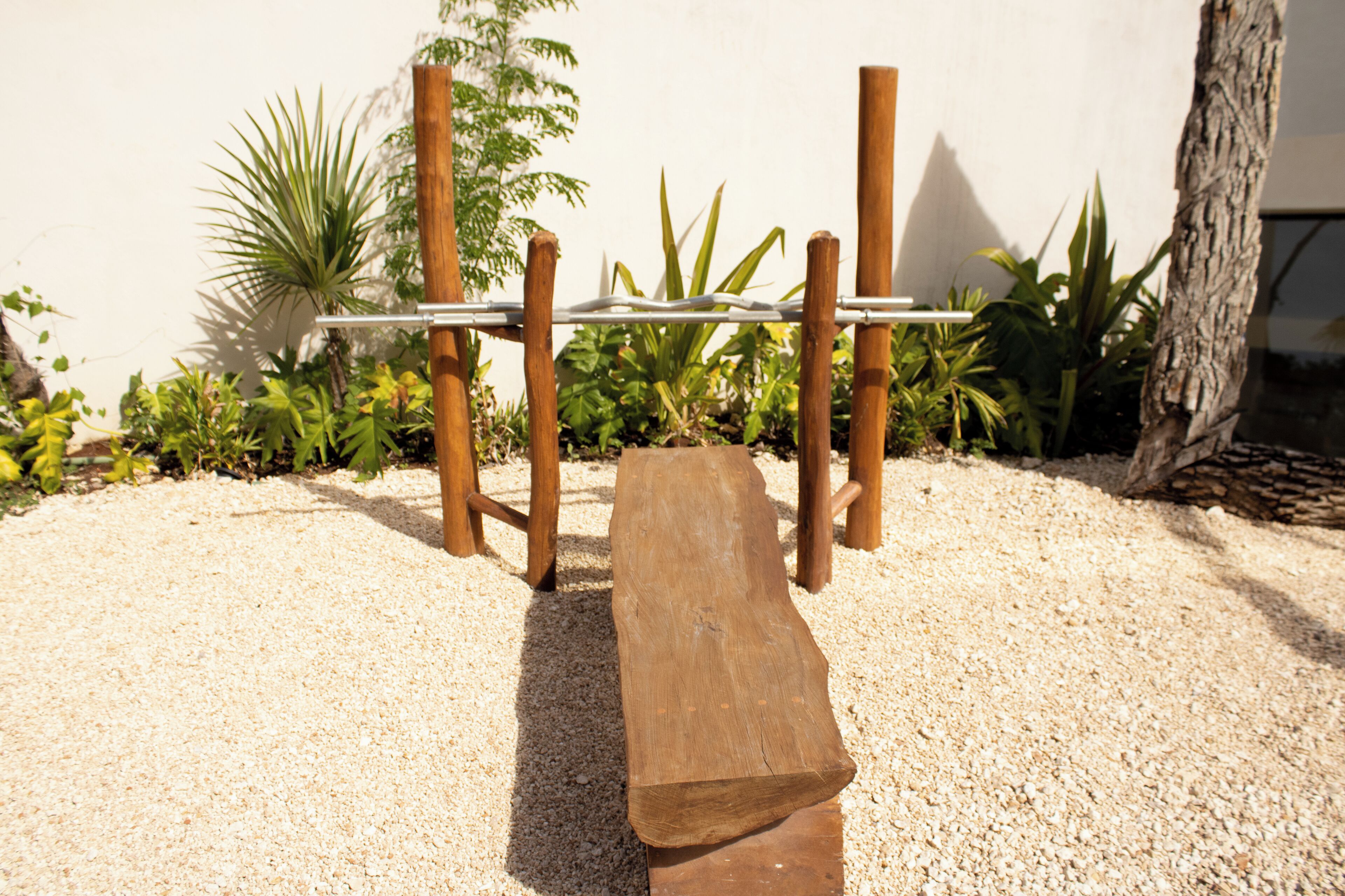 Un banco de madera con estructura metálica, rodeado de grava y plantas.