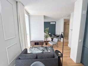 Un salon moderne avec un canapé gris, un coin repas comprenant une table et des chaises, et un couloir menant à une autre pièce.