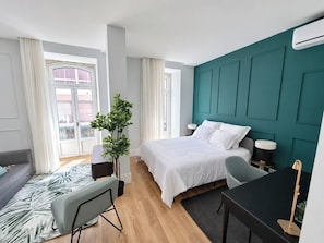 A modern hotel room with a bed, a desk, a chair, a potted plant, and a view of the outside. - Studio 201 • Lisbon • Balcony • Elevator • WiFi (Lisbon)
