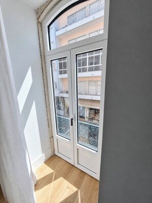 A room with a large window, a staircase, and a view of a building with balconies. - Studio 201 • Lisbon • Balcony • Elevator • WiFi (Lisbon)