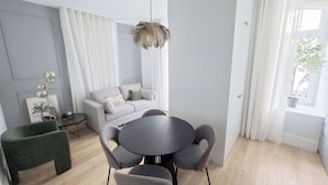 Un salon moderne avec un canapé gris, une table de salle à manger ronde entourée de chaises grises, une petite table d’appoint et un luminaire suspendu.