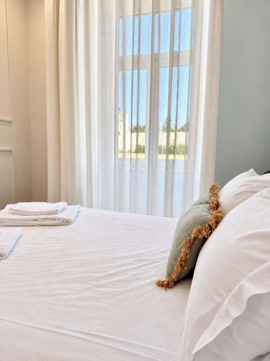 Habitación de hotel con cama, cortinas blancas y vistas al exterior.