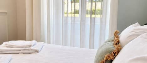 Een hotelkamer met een bed, witte gordijnen en uitzicht op het omliggende landschap.