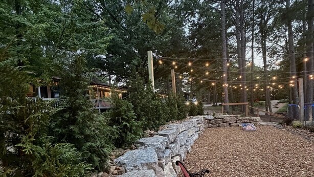 En sti af sten fører til en træbænk i et skovområde med lyskæder.