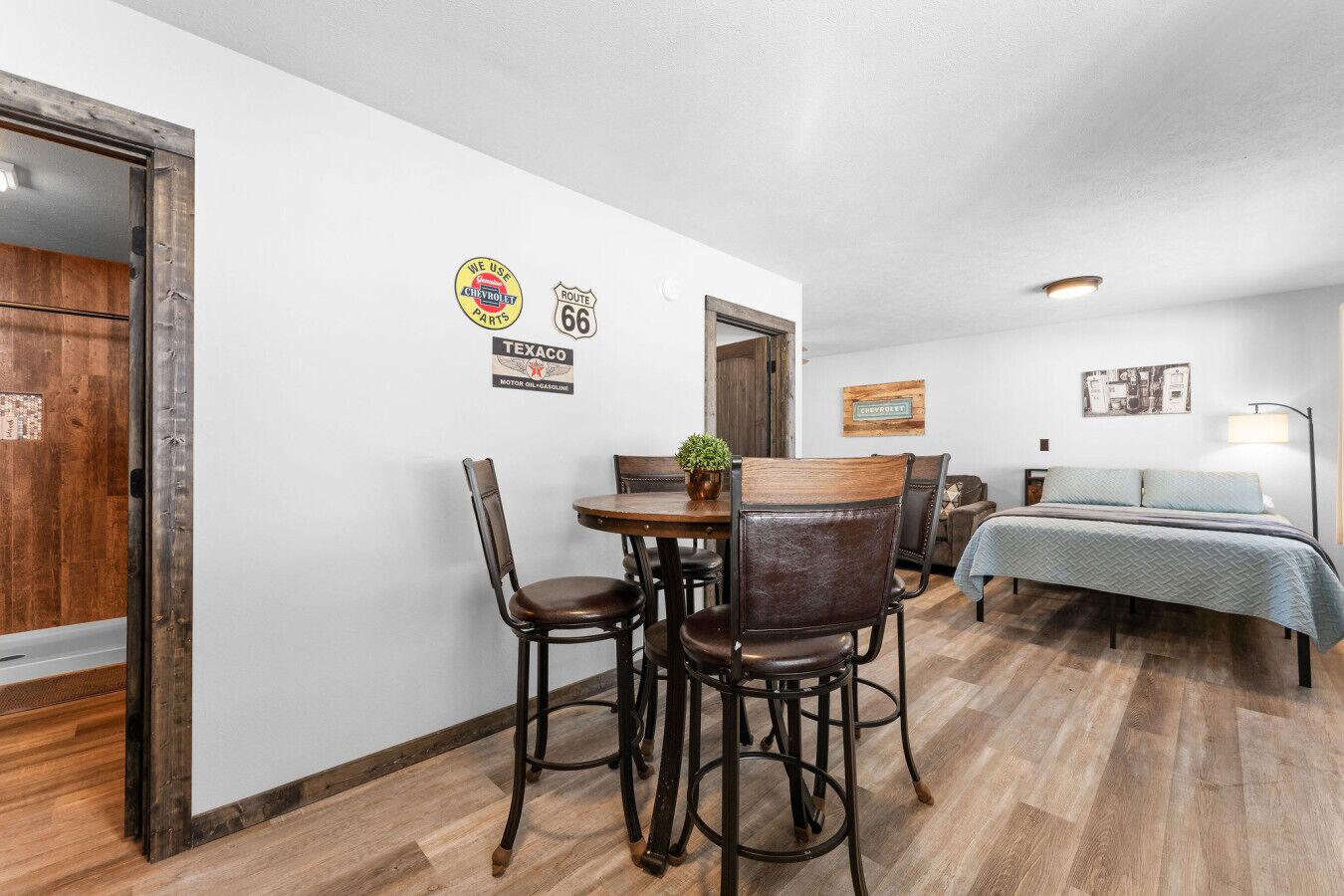 Une pièce de taille modeste, avec une table et des chaises en bois, un lit recouvert d’une courtepointe bleue et une lampe fixée au mur.