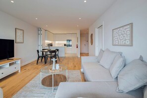 A modern living room with a sofa, TV, and dining area. - Serenity Suite I (Setúbal)