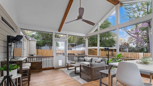 Une terrasse couverte avec un plancher en bois, un ventilateur de plafond et de grandes fenêtres donnant sur le jardin.
