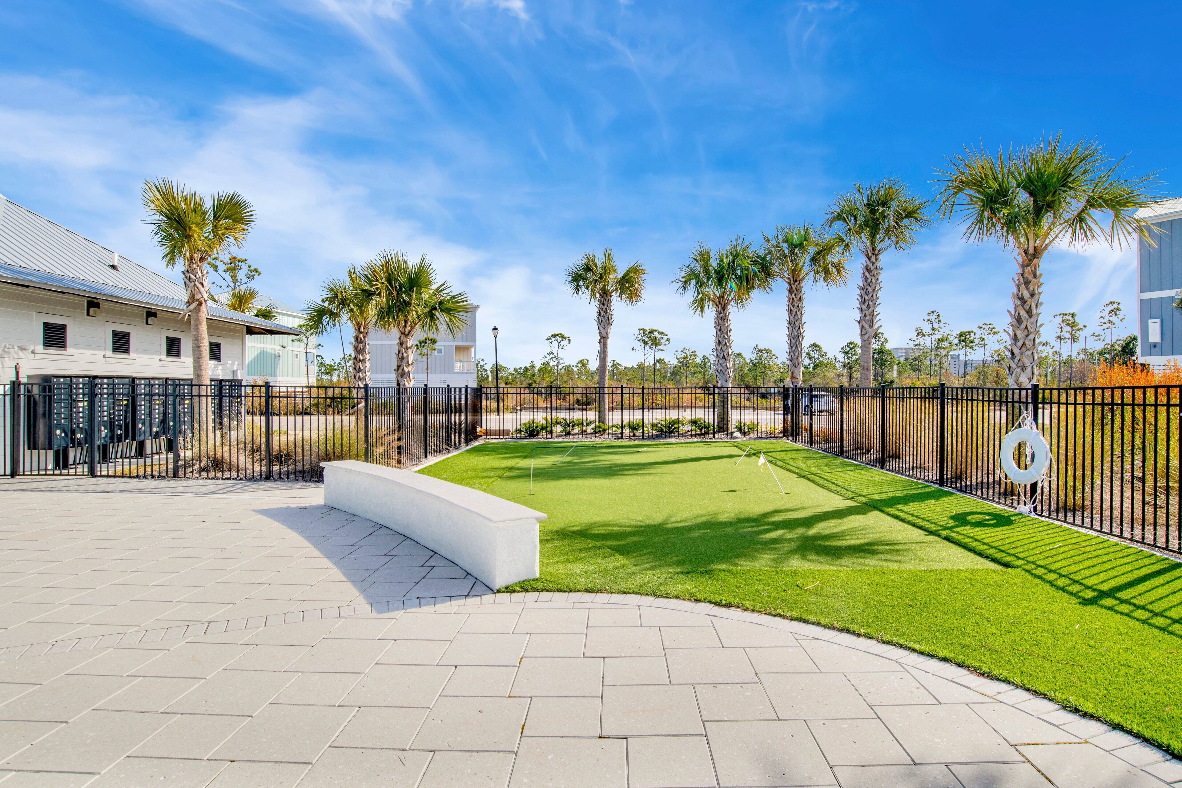 A golf course with a well-maintained green, palm trees, and a paved walkway.