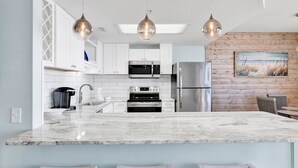 A modern kitchen with white cabinets, stainless steel appliances, a marble countertop, and pendant lighting. - Beachfront 1BR @ Phoenix X • Sleeps 4 • Gulf Views & Next to Flora-Bama (Orange Beach)