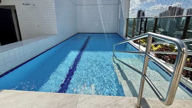 A rooftop swimming pool with clear blue water, surrounded by white tiled walls and metal railings. - Flat Jardins da Madalena (Recife)