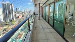 A modern building with a glass facade, a balcony with metal railings, and a view of a cityscape with high-rise buildings. - Flat Jardins da Madalena (Recife)