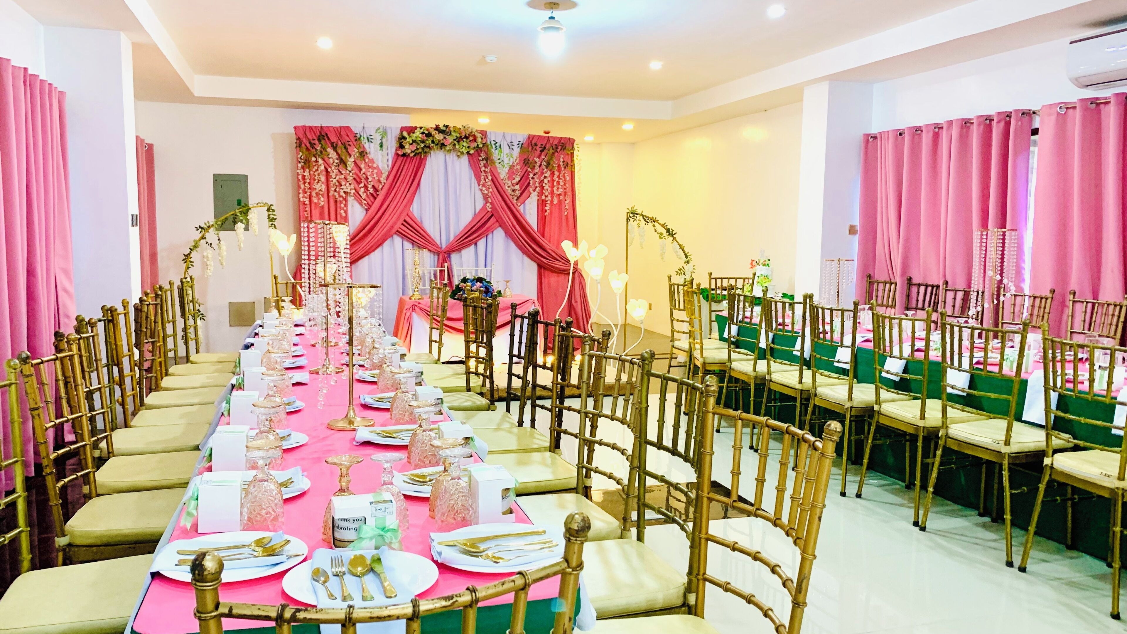 Une salle de banquet avec de longues tables, des chaises dorées et des rideaux roses.