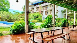 Un espacio al aire libre con bancos de madera, piscina y abundante vegetación.