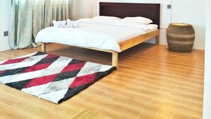 Un dormitorio moderno con techo de madera, cama con ropa de cama blanca, dos luces fijadas a la pared y un tapete estampado.