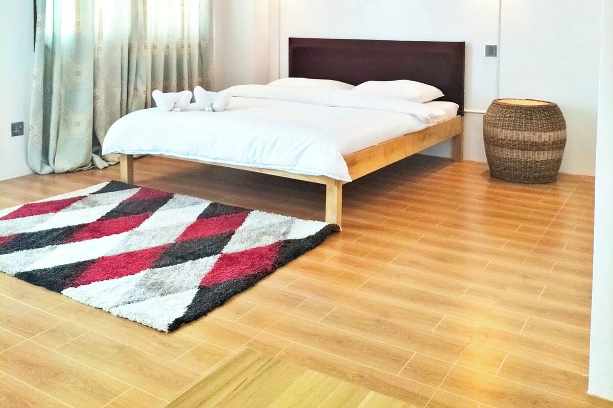 A modern bedroom with a wooden ceiling, a bed with white bedding, two wall-mounted lights, and a patterned rug.