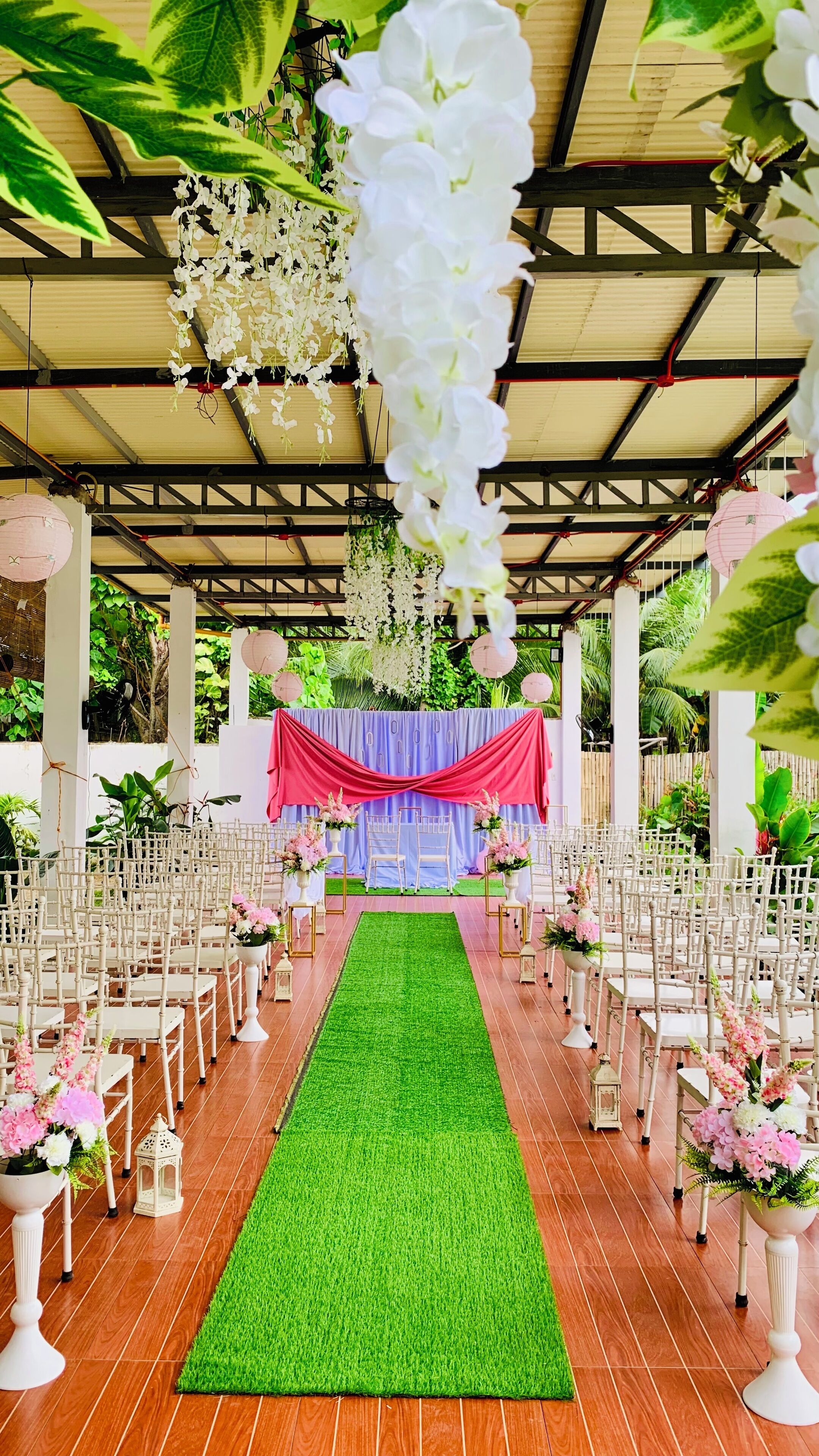 An aisle with white chairs and a green carpet, leading to a stage with a red and blue backdrop.