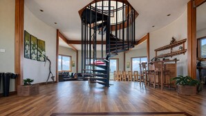 Un vaste espace de vie agrémenté d’un escalier en colimaçon central, de parquets en bois et d’une vue sur l’extérieur.