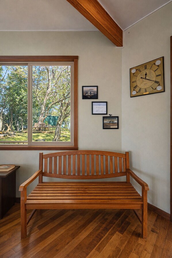 A wooden bench in a room with a large window, a wall-mounted clock, and framed certificates.