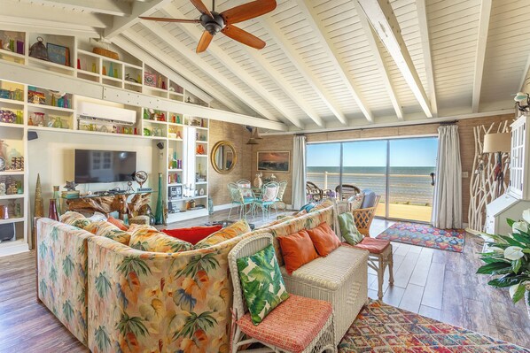 A spacious living room with a large sofa, a dining area, and a view of the beach through large windows.