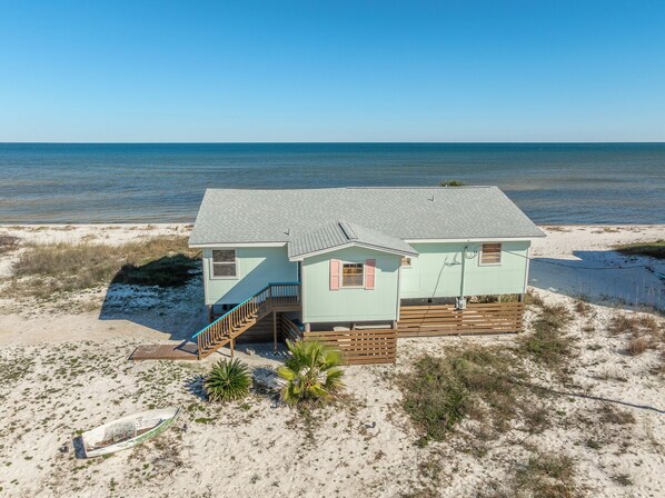Een strandhuis met twee verdiepingen, een houten terras en een trap naar de bovenverdieping.