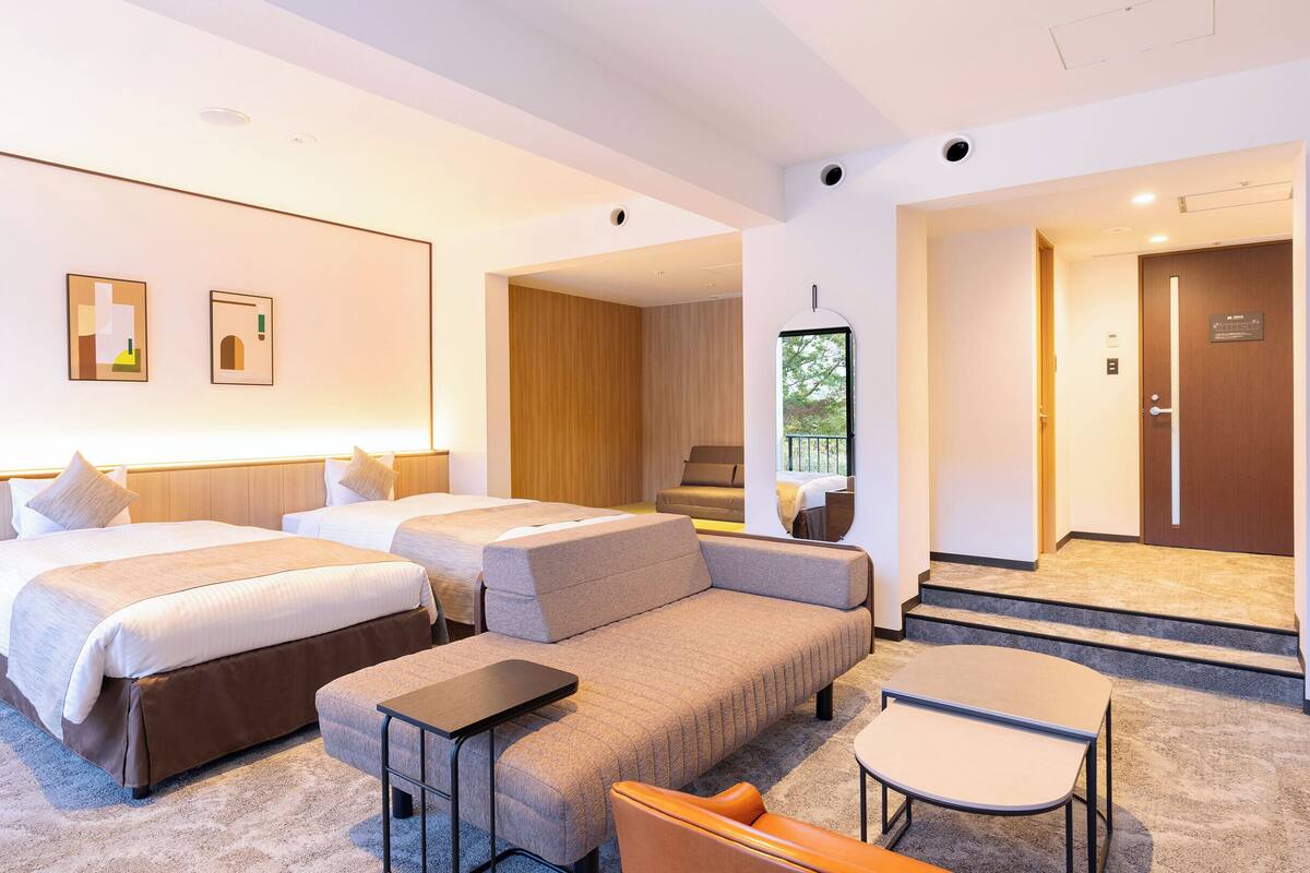 Una habitación de hotel moderna con dos camas, un sofá, una mesita y vistas al exterior.