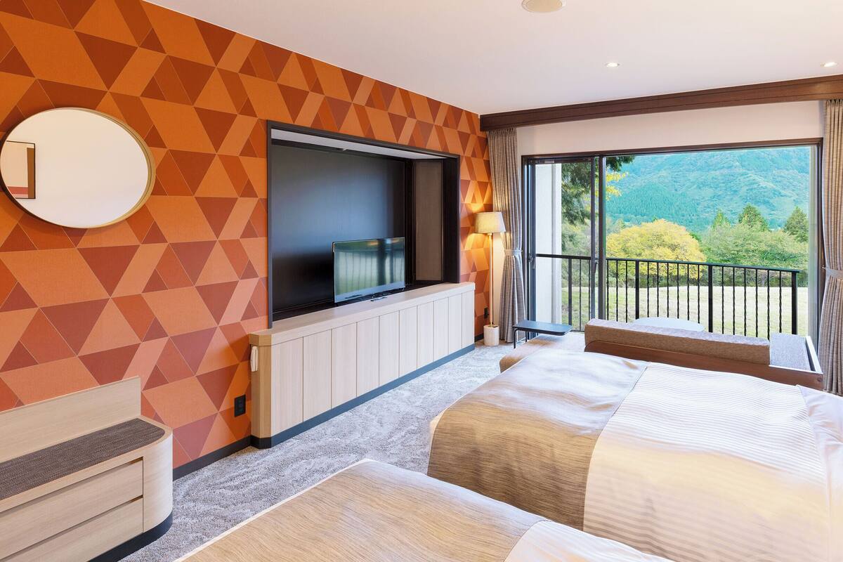 Habitación de hotel con una cama grande, televisión, balcón con vistas a zonas verdes y una pared con diseño geométrico.