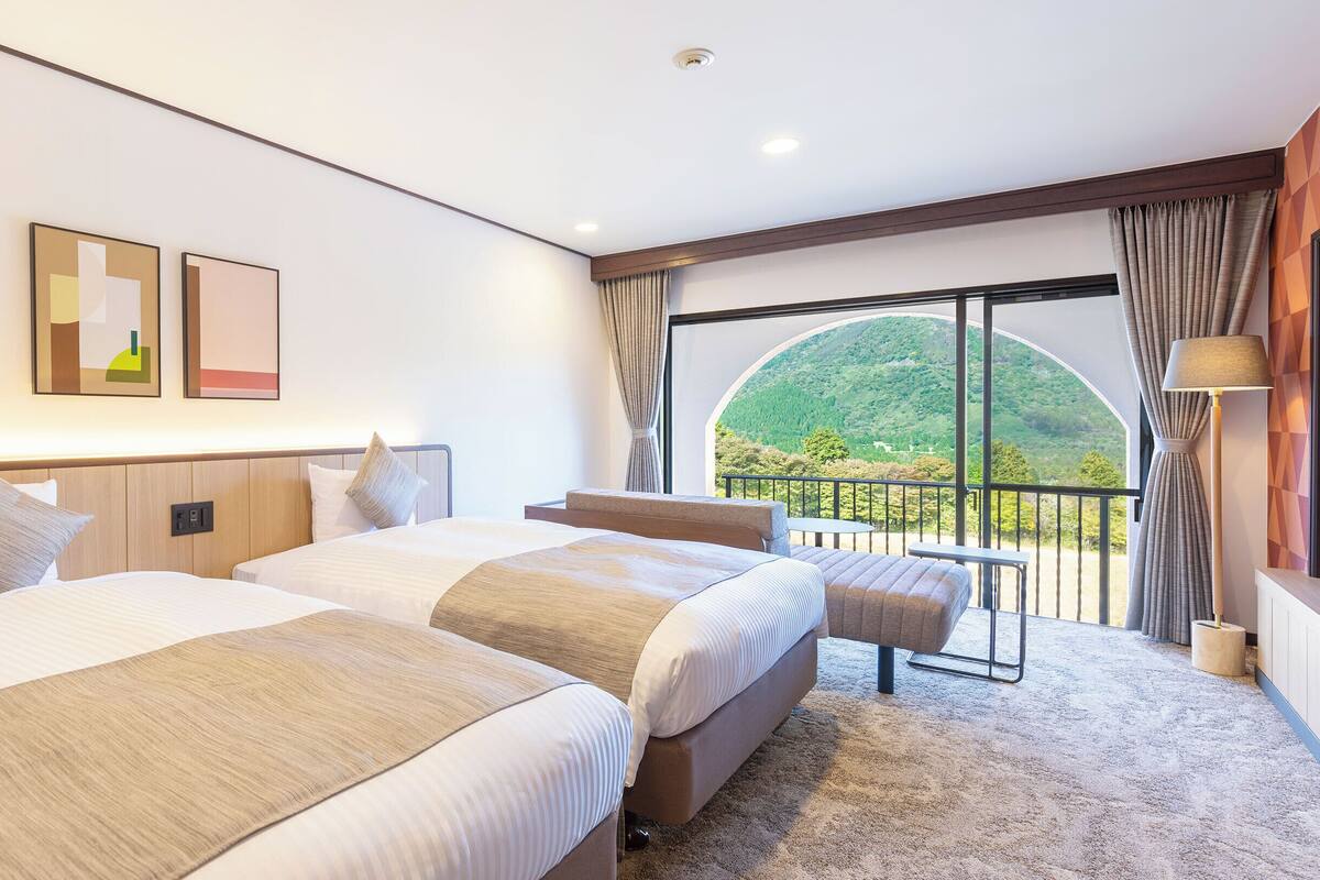 Una habitación de hotel con dos camas, un balcón con vistas a un paisaje verde y un diseño moderno.