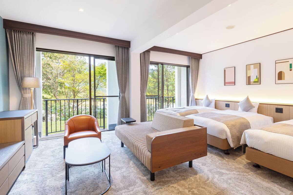 Una habitación de hotel moderna con una cama grande, un sofá, un escritorio y un balcón con cortinas.