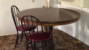 A dining table with four chairs, a white wall, and a ceiling-mounted air conditioner.