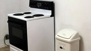 A compact kitchen with a stove and a trash can.