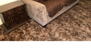 Un canapé marron recouvert d’un tissu matelassé, dans une pièce où se trouve un tapis marron.