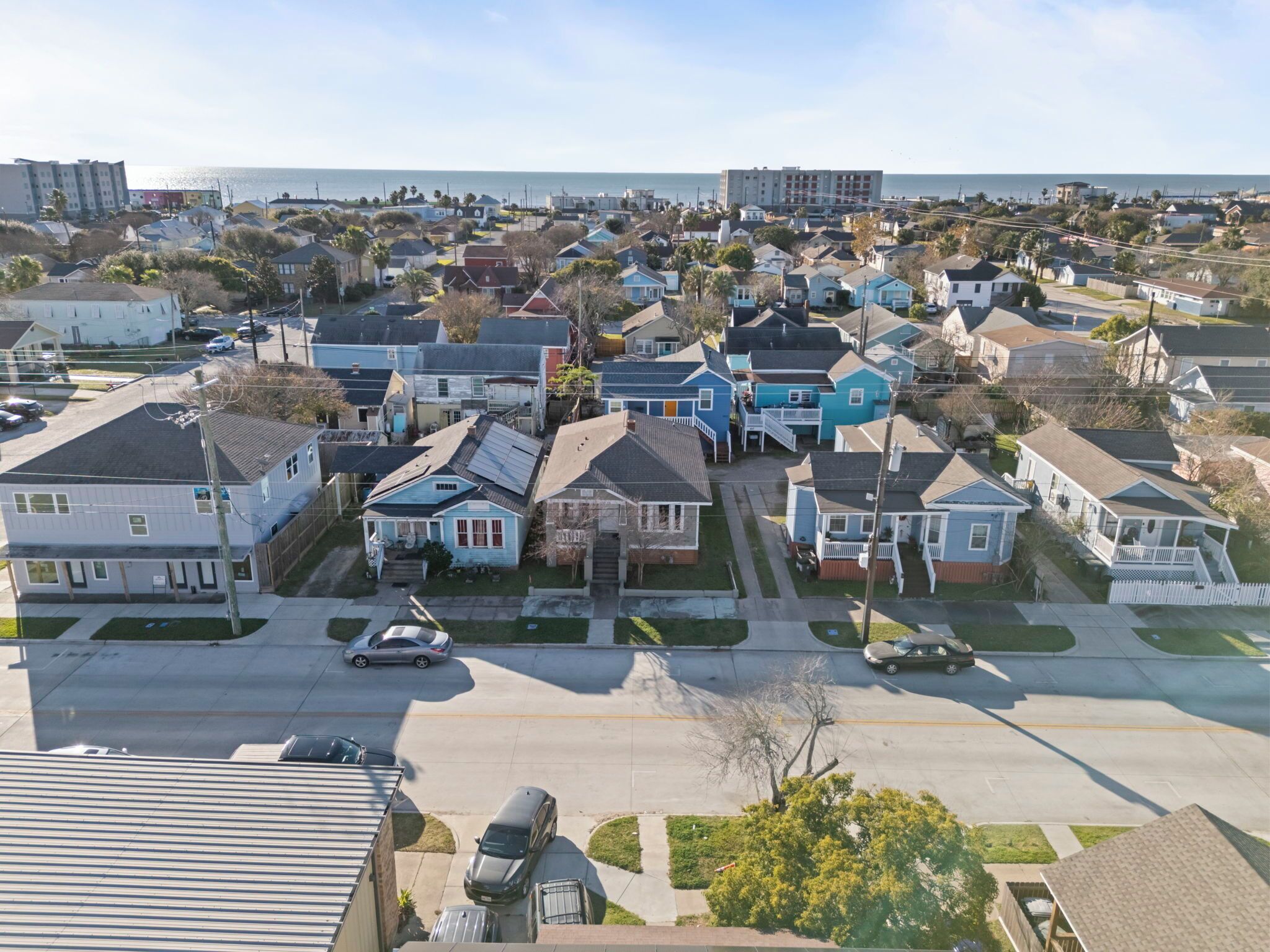 A residential area with houses, a road, and a beach in the background.