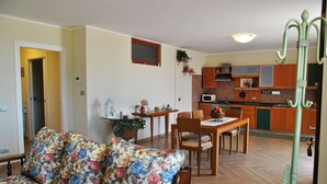 Ein Wohnzimmer mit floraler Couch, einem Esstisch mit Stühlen und einer Küchenzeile mit Holdekor und Mikrowelle.