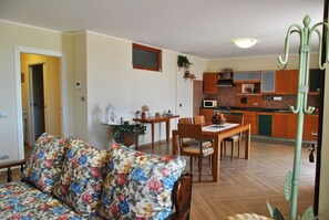 A living room with a floral sofa, a dining table with chairs, and a kitchen area with wooden cabinets and a microwave. - Villa Saturnia between nature and the sea (Spigno Saturnia)