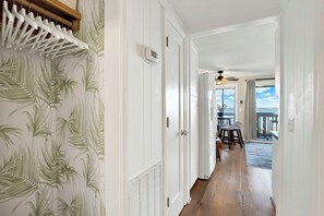 A hallway with a white door, a thermostat, and a view of a balcony with a table and chairs. - Serene Tybee Retreat with Ocean Views | Heated Pool Access (Tybee Island)