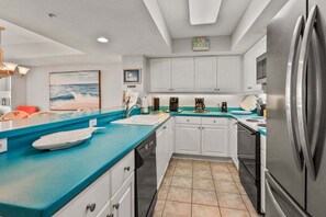 A modern kitchen with white cabinets, a blue countertop, and a stainless steel refrigerator. - Ocean Bay Club 107 | Oceanfront 4BR Condo | Steps to Main St & Beachfront Pool (North Myrtle Beach)