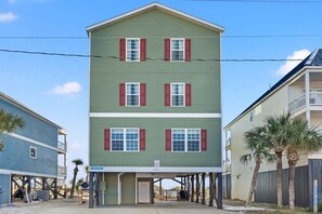 A multi-story building with a flat roof, red shutters, and a balcony on the second floor. - Oceanfront vacation rental with pool, hot tub, and game room—perfect for families and groups (North Myrtle Beach)