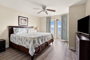 A bedroom with a bed, a ceiling fan, a TV, and a view of the outdoors. - Oceanfront vacation rental with pool, hot tub, and game room—perfect for families and groups (North Myrtle Beach)