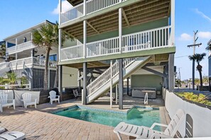 A multi-story building with a pool area, outdoor seating, and a staircase leading to the upper levels. - Oceanfront vacation rental with pool, hot tub, and game room—perfect for families and groups (North Myrtle Beach)