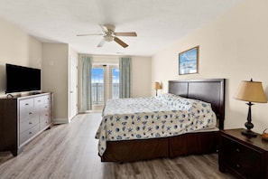 A hotel room with a bed, a television on a dresser, a ceiling fan, and a view of the outdoors through a door. - Oceanfront vacation rental with pool, hot tub, and game room—perfect for families and groups (North Myrtle Beach)