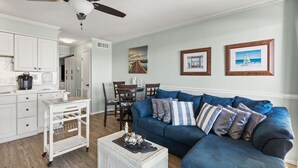 A living room with a blue sofa, white coffee table, and a dining area with a table and chairs. - Direct oceanfront luxury on the 1st floor—step from balcony to beach in seconds (North Myrtle Beach)