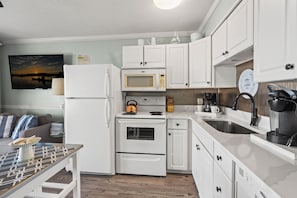A modern kitchen with white cabinetry, a microwave, a kettle, and a coffee maker. - Direct oceanfront luxury on the 1st floor—step from balcony to beach in seconds (North Myrtle Beach)