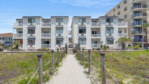 Ett hotell som ligger direkt vid stranden, med en sandgång som leder till entrén. Hotellet har flera balkonger och en modern arkitektonisk design.