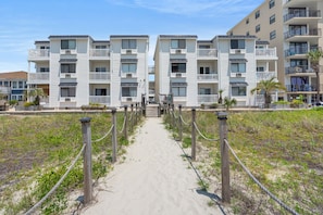 A beachfront hotel with a sandy walkway leading to the entrance, featuring multiple balconies and a modern architectural design. - Cozy side-view ocean condo with balcony, pool access, and easy beachside living (North Myrtle Beach)