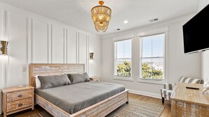 A bedroom with a wooden bed, a nightstand, a TV, and a large window with blinds. - Exceptional luxury retreat steps from the beach with outdoor oasis, heated pool, elevator (North Myrtle Beach)