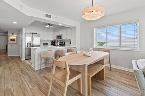 A modern kitchen with white cabinets, stainless steel appliances, and a wooden dining table with chairs. - Oceanfront condo w/pool, lazy river, & family fun steps from the beach (North Myrtle Beach)