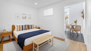 A bedroom with a bed, bedside tables, a bench, a dining area with chairs, and a window. - Matosinhos Coastal Breeze Studio (Matosinhos)