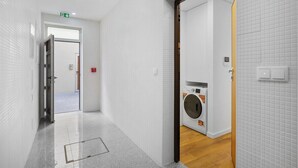 A hallway with a washing machine, white tiled walls, and a door leading to another room. - Matosinhos Coastal Breeze Studio (Matosinhos)