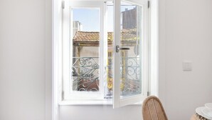 A room with a white door leading to a balcony with a wrought iron gate and a view of a building with a tiled roof. - Matosinhos Coastal Breeze Studio (Matosinhos)