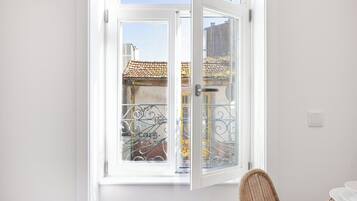 Una habitación con una puerta blanca que da a un balcón con reja de hierro forjado y vista a un edificio con tejado de tejas.